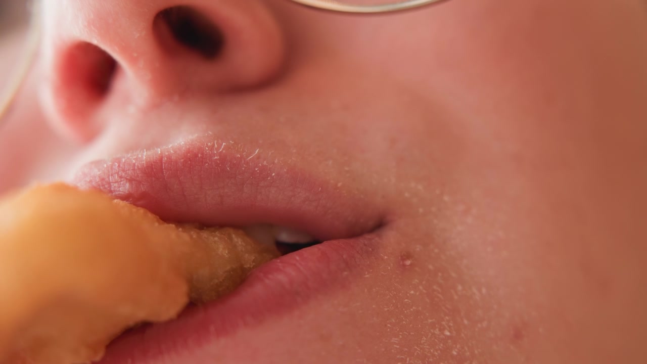Tampilan makro ekstrem pada wajah bagian bawah menunjukkan mulut menggigit camilan goreng, bibir terbuka, lidah menyentuh makanan, lalu bibir tertutup dengan remah dan kelembapan tertinggal di dagu, menciptakan detail makanan yang sangat dekat.