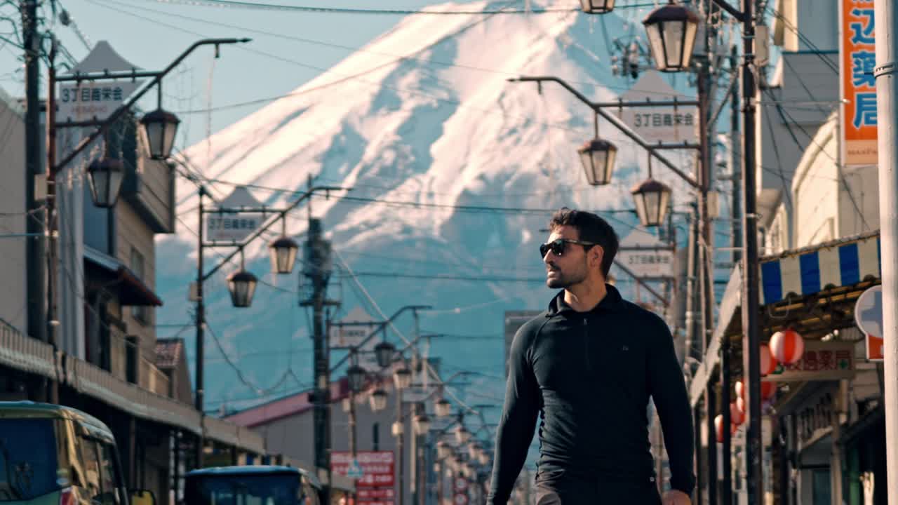A man walks along Honcho Street in Fujiyoshida, Japan, with the breathtaking Mount Fuji rising in the background.