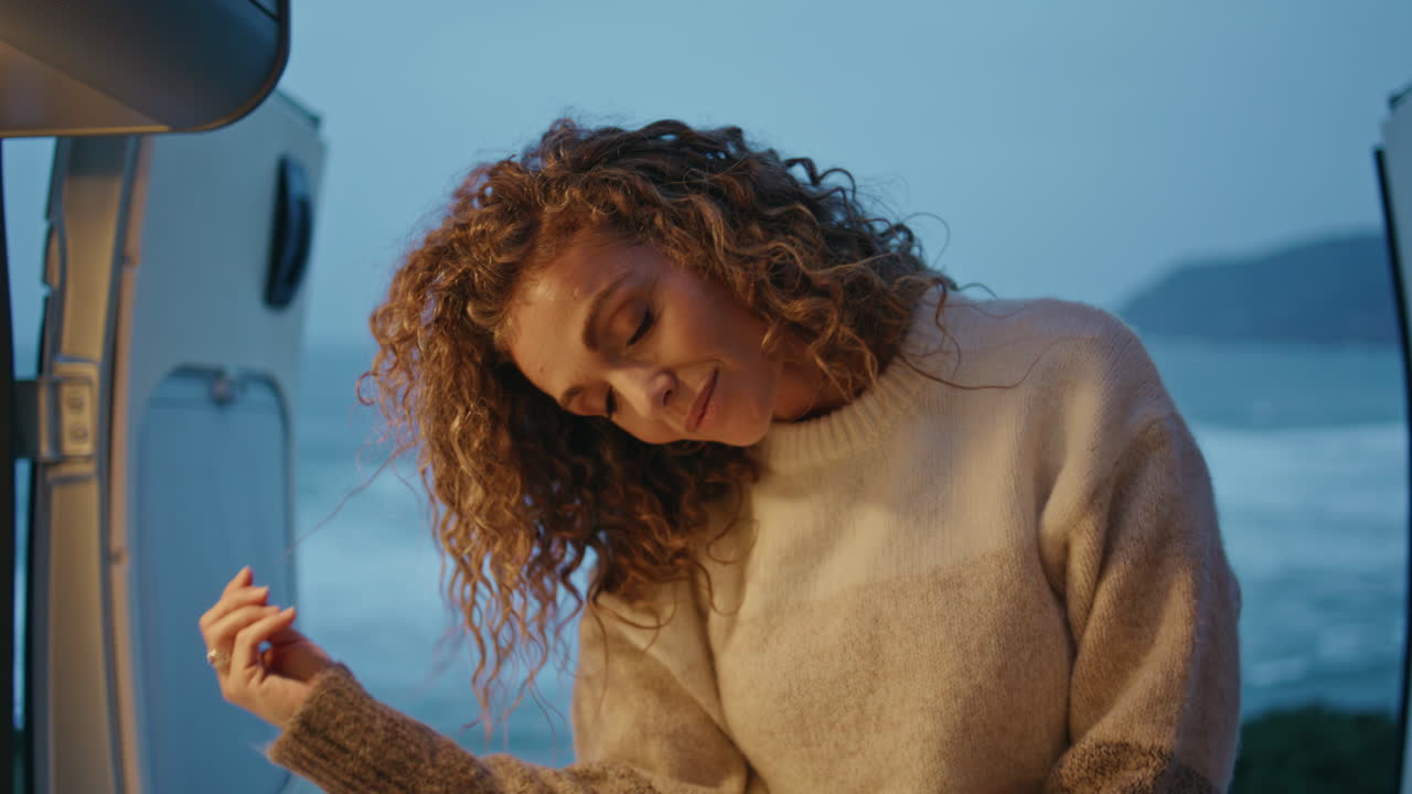 romántico viajero posando por la noche en la costa del océano sentado en una caravana de cerca.