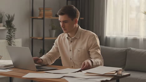 man working on a laptop at a desk with documents