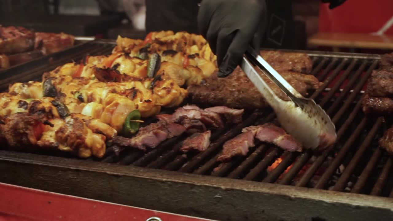 Carne di pecora biologica naturale che cuoce all'aperto su un barbecue a legna e carbone durante un festival tradizionale della carne, primo piano dello chef che gira la carne sulla griglia per una cottura uniforme