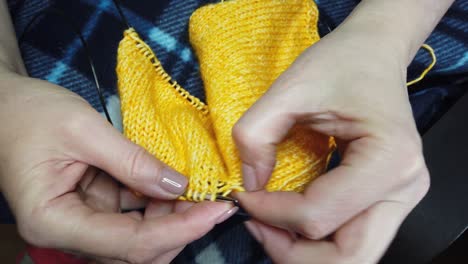 women's hands knit woolen jacket with knitting needles. top view, close-up of hands and knitting.