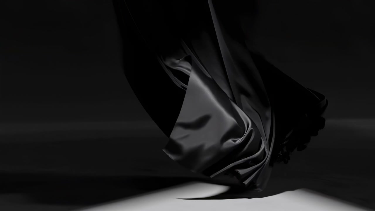 Dark abstract close-up of glossy black fabric with soft flowing folds, a bright surface along the bottom edge, and strong side lighting in a minimal studio