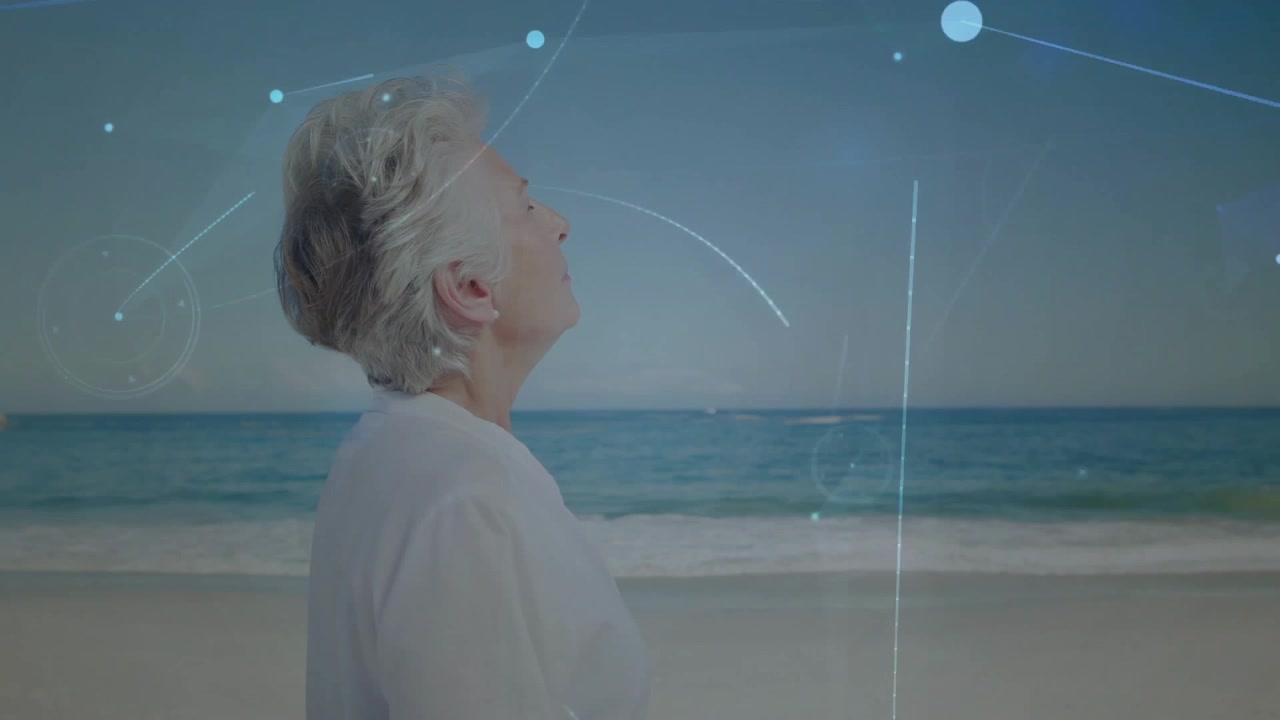 Senior woman standing beach looking horizon, initiating network swirling around torso for tech