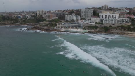 Bondi-Icebergs-Pool-At-Bondi-Icebergs-Club-In-Eastern-Suburbs-With-People-On-Foamy-Waves-Of-Bondi-Beach-In-Sydney,-NSW,-Australia