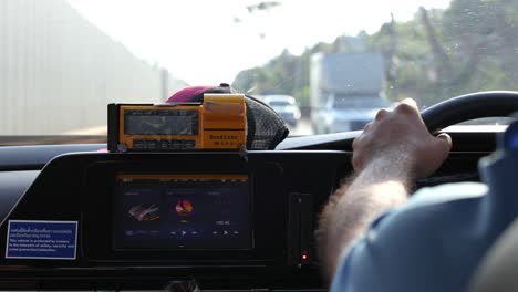 View from inside a car driving through Phuket, Thailand. Daytime, clear weather, dashboard visible, hands on steering wheel