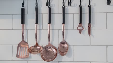 copper kitchen utensils hang neatly on a tiled white wall, catching natural light in a minimal, modern cooking space.