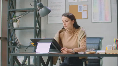 Young-Woman-Sitting-at-Her-Desk-She's-Drawing-Writing-and-Using-Pen-with-Digital-Tablet-Computer.-Hands-with-Pen