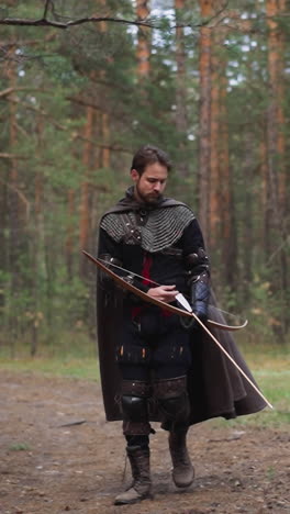 hombre con traje de guerrero medieval con arco camina a lo largo del bosque de coníferas en cámara lenta. reconstrucción de una vieja batalla. período de la edad media