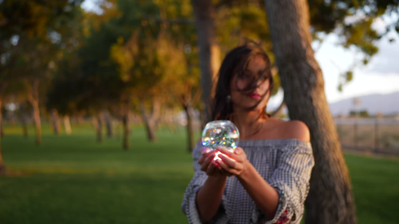 Un hermoso hechicero sosteniendo una bola de cristal mágica y brillante con una mirada encantadora y misteriosa.