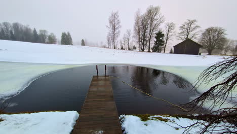 Winter-snowed-landscape-of-a-bridge-with-small-lake-of-water,-dry-trees-slow-motion-feeling,-countryside,-snow-panoramic-white-skyline,-autumn-at-European-village