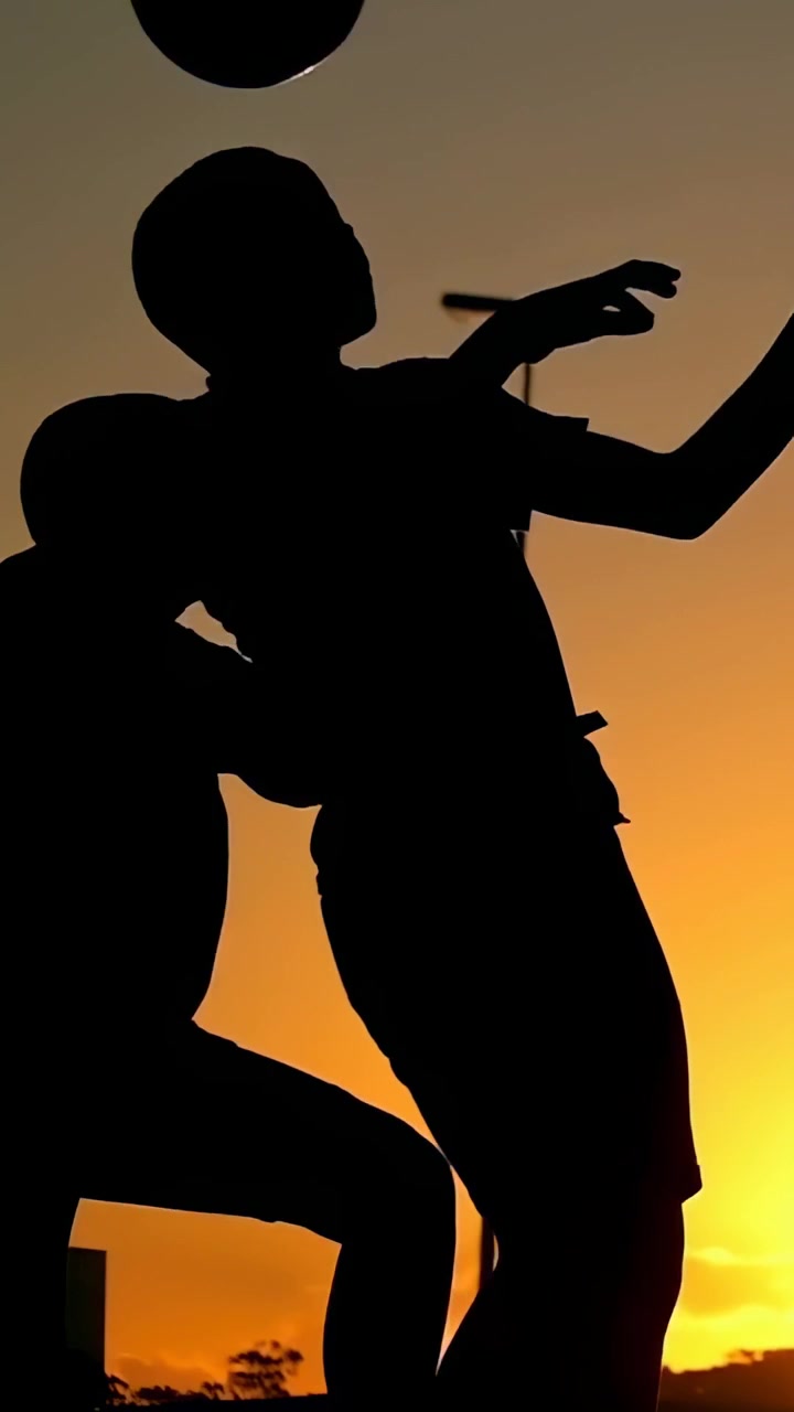 Video verticale: Un adolescente alto e chinato che guida dei ragazzi che corrono lungo la strada al tramonto per giocare, con un lampione.