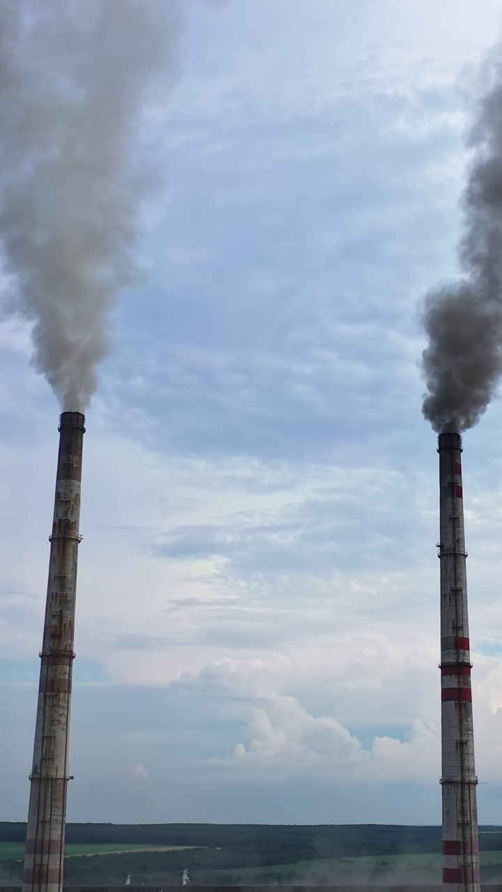 High chimney pipes with grey smoke from plant. Smoke stack with harmful emissions against blue sky. Plant pipes pollute atmosphere. Industrial factory pollution, smokestack exhaust gases. Vertical video