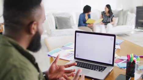 hombre afroamericano haciendo llamada de video portátil, espacio de copia en la pantalla, colegas detrás, cámara lenta