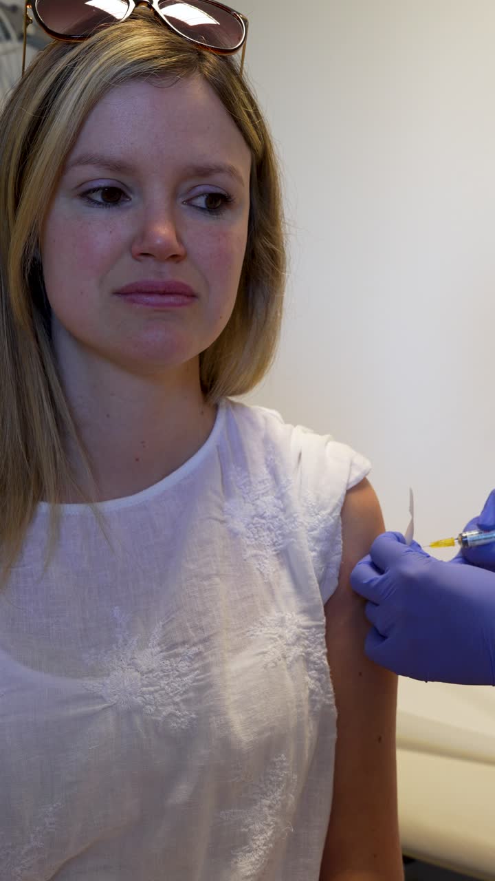 Calm caucasian woman gets vaccination in arm through syringe injection, vertical