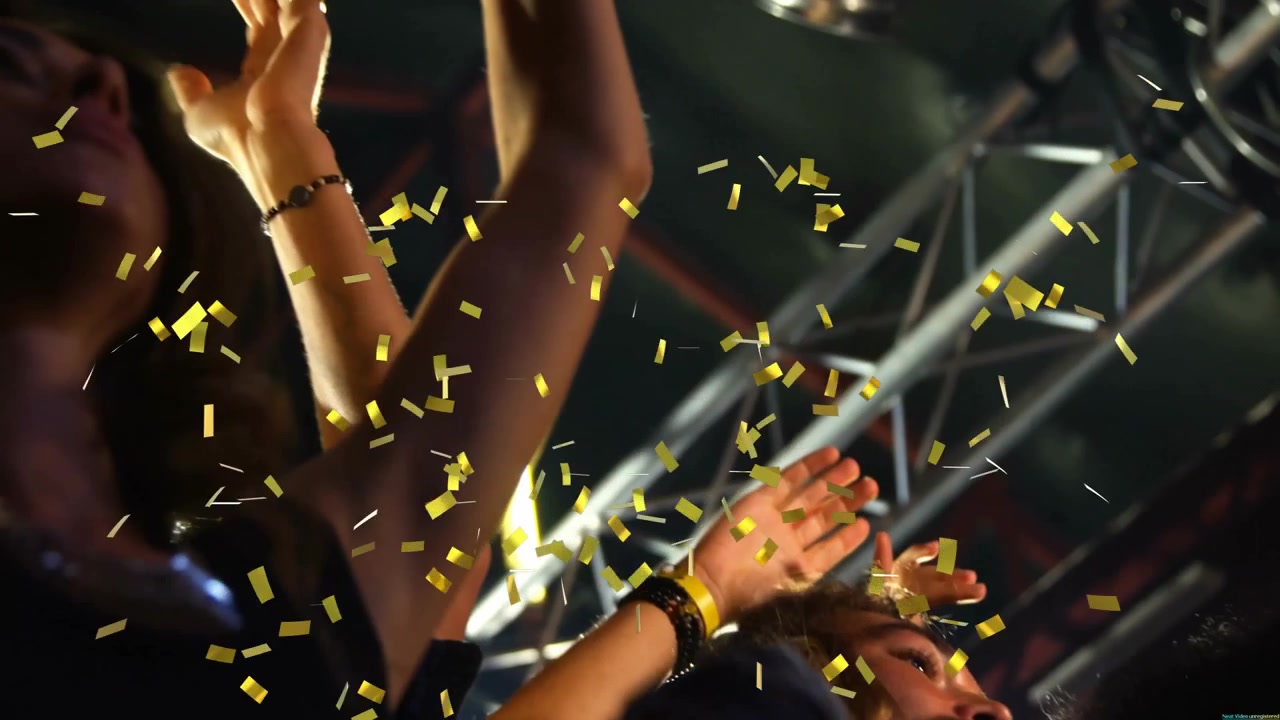 Friends reacting to gold confetti raising arms and clapping at concert under metal truss lights