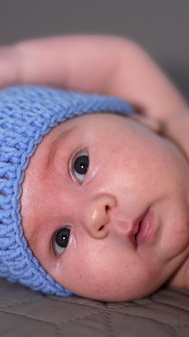 Small kid lying and moving his tiny hands quickly. Adorable babe in funny blue doggy cap and knitted bone. Beautiful child in the bedroom. Vertical video