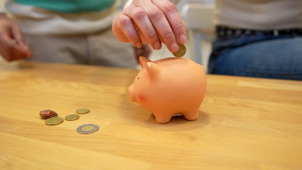Hand Putting Euro Coins into a Pink Piggy Bank