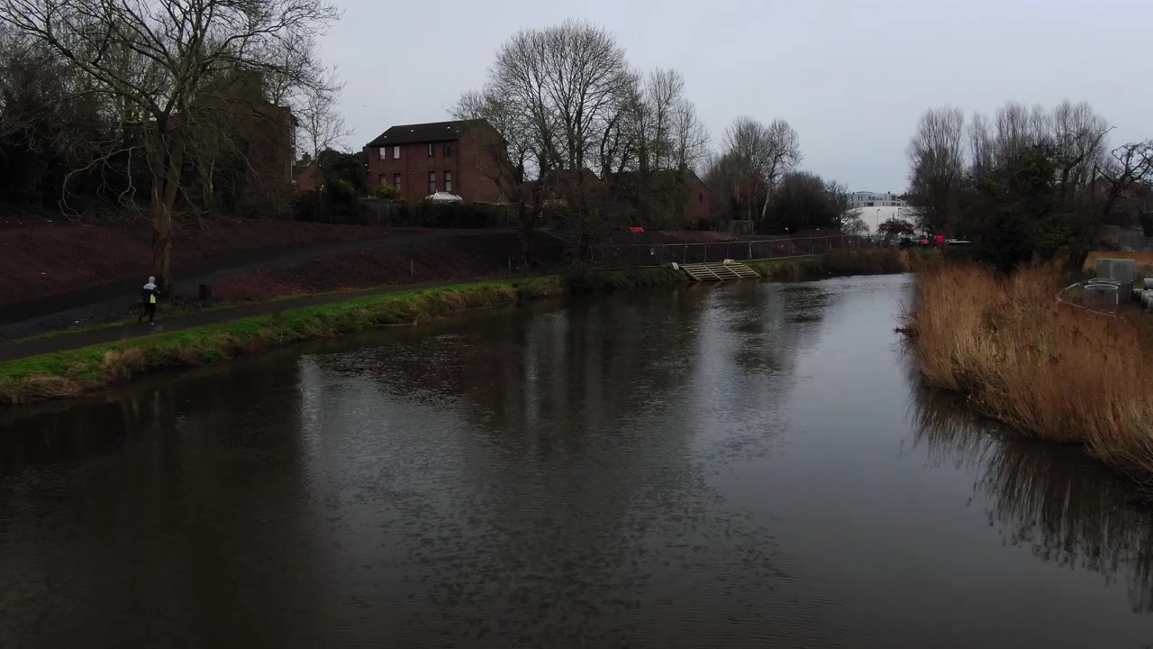 Drone shot of a man running along a river path
