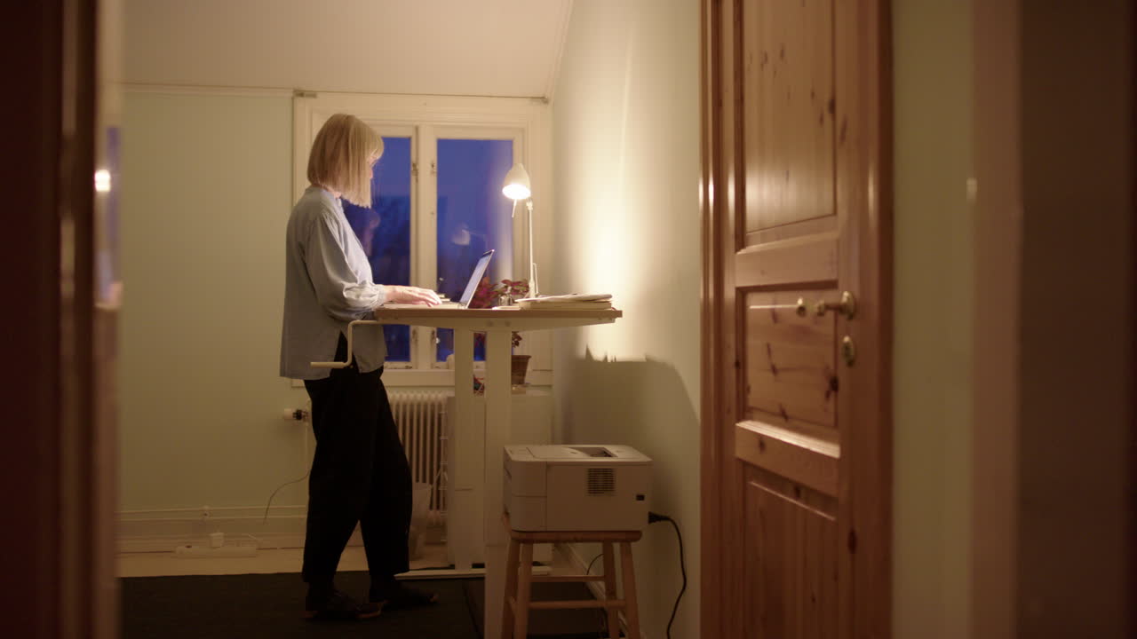 Woman hustling online on laptop at night use standing desk for improved posture