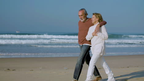 happy senior couple hugging while walking along ocean coast