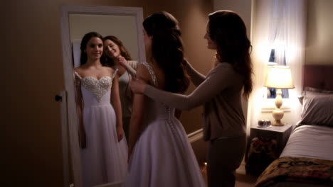 woman tries on a white, sparkling dress with assistance in a bedroom