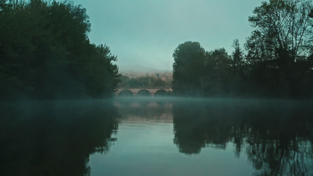 안개가 자욱한 아침에 돌다리가 있는 강 위를 날다