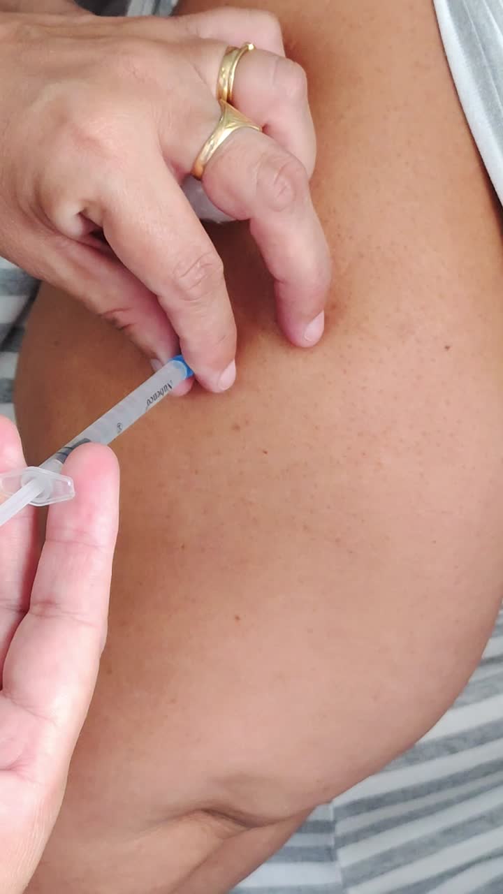 Primo piano delle mani di un'infermiera che somministrano un vaccino sul braccio di una donna.