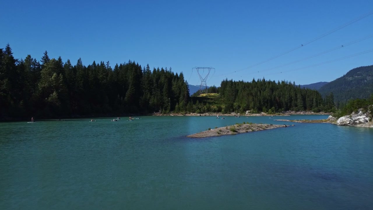 aerial view over emerald lake in mountainous region paddle boarders standing on boards in water paddling along this peaceful blue coloured lake in whistler bc approach low altitude
