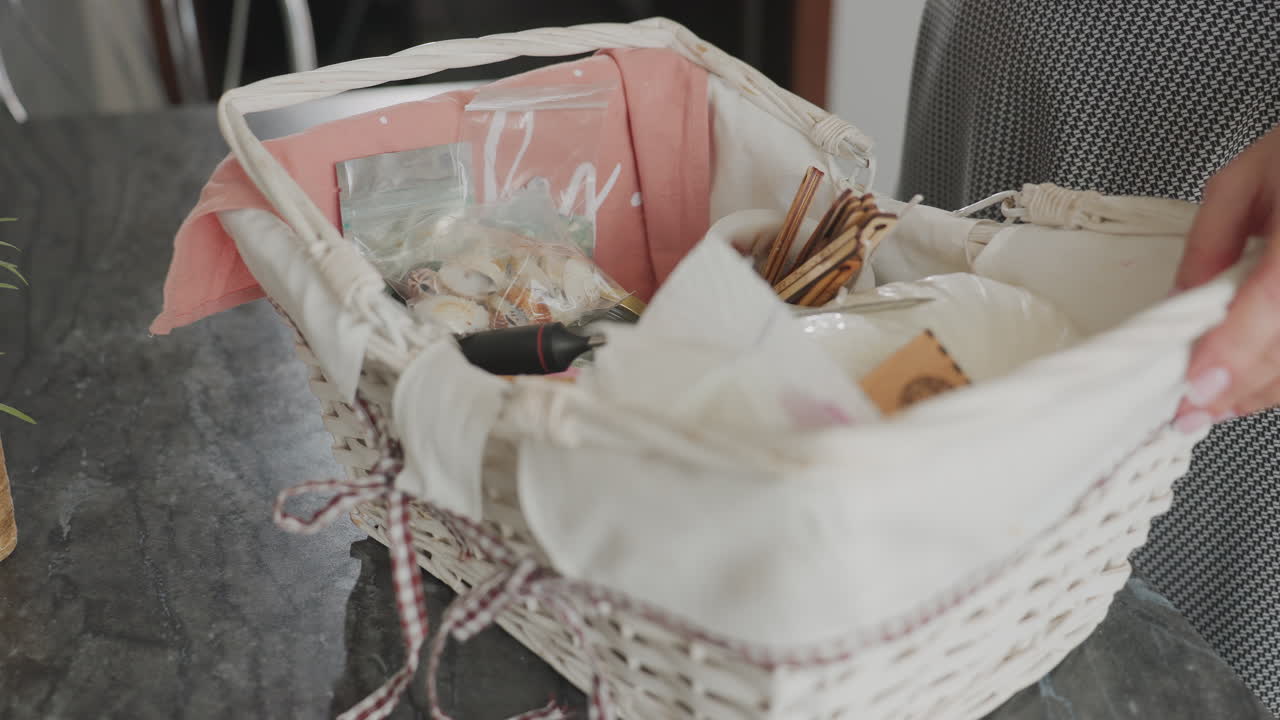 Close up of girl in plaid dress dropping white gift basket filled with various items onto dark marble table removing items one by one and placing them on surface