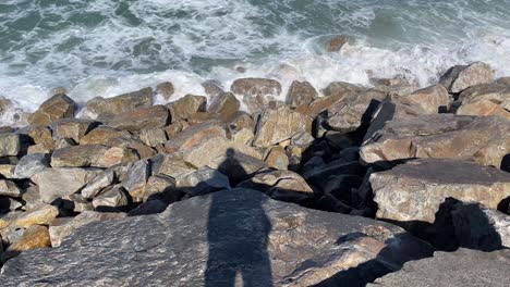 shadow of a man looking to the waves crushing on rocks