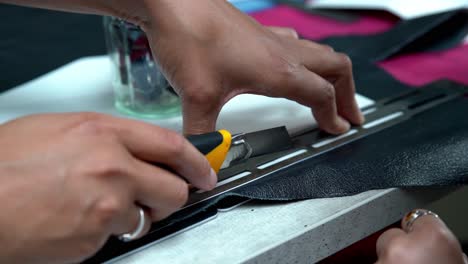 female workers cutting leather segments for crating a handbag using a guide ruler, handheld closeup shot