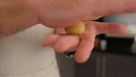 primer plano de un pastelero haciendo rodar una bola de masa para galletas en sus manos