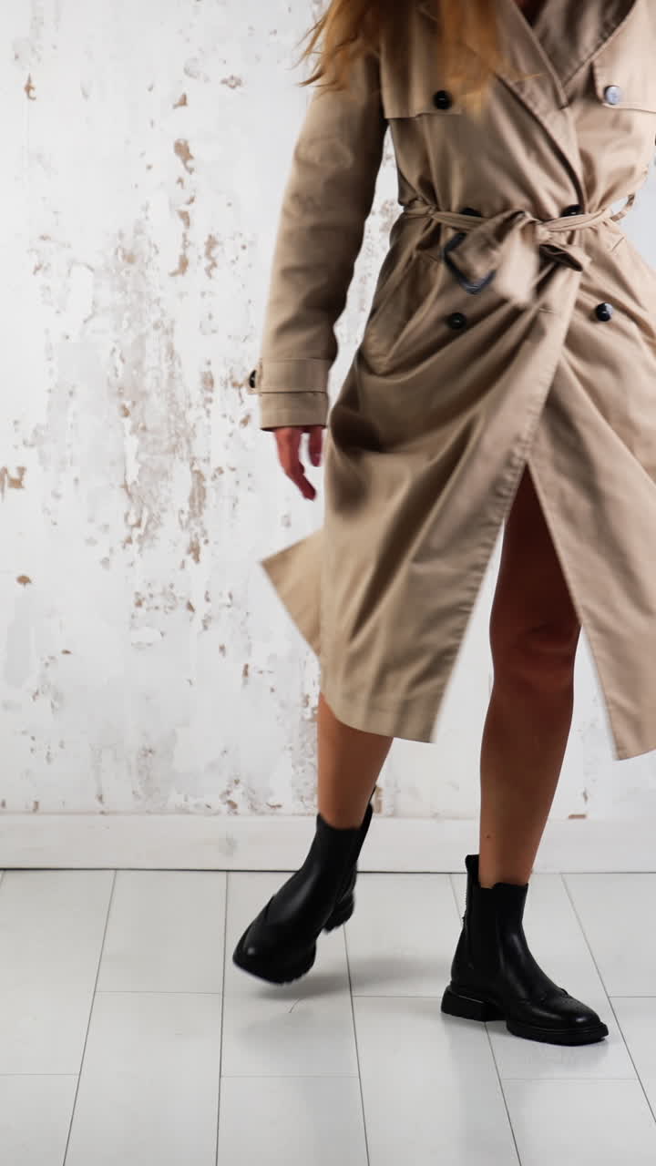 Modern clothes and stylish footwear demonstration. Model wearing beige coat and black tractor boots posing in the studio. Vertical video