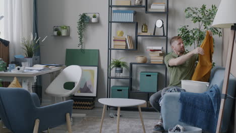 man putting away clothes on a couch in a messy living room