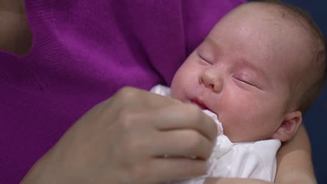 caring mother cleaning baby's mouth with a napkin. kid grimaces as doesn't like cleaning his face. close up.