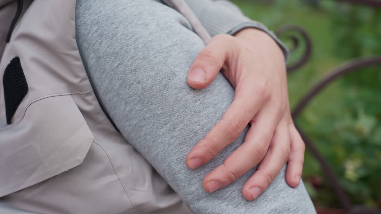 Close up of hand gently rubbing another person leg warmly in outdoor setting, both dressed in casual cozy outfits, conveying comfort, affection, and tenderness with soft focus greenery in background