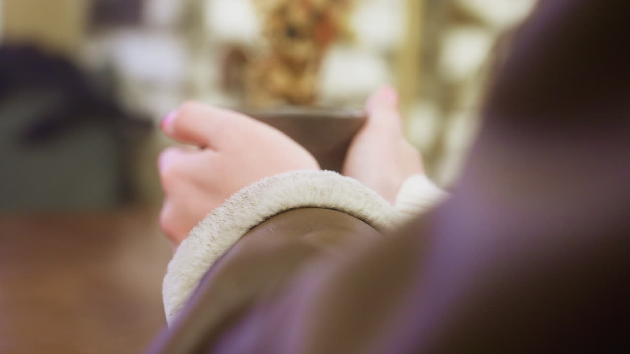 Close-up shot of coffee cup held by woman's hand with blurred background, focusing on the warmth of the beverage and cozy cafe setting, capturing a peaceful and intimate moment