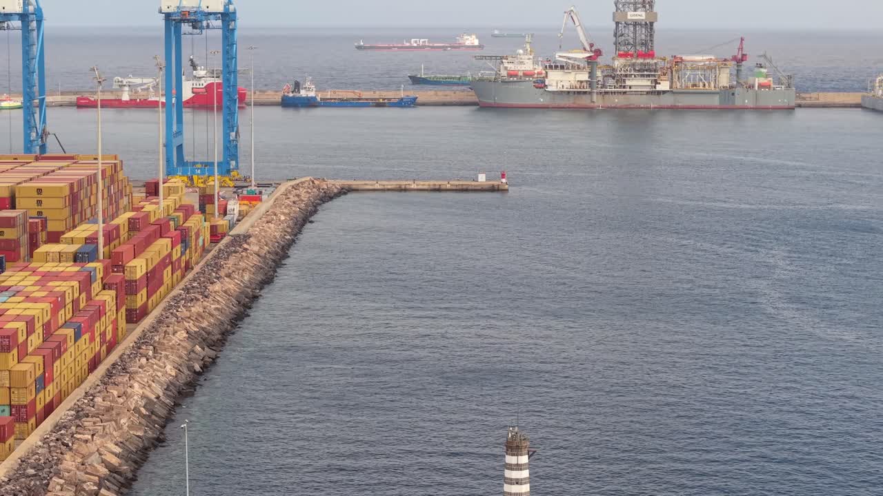 Veduta industriale del Porto di La Luz con container merci impilati sul molo e varie imbarcazioni che navigano nel calmo oceano Atlantico