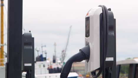 Electric-car-charging-station-system-on-a-city-street,-a-cable-connected-to-a-car,-future-of-the-automobile,-clean-sustainable-energy,-overcast-day,-medium-shot,-defocused-bussy-Port-Of-Liepaja