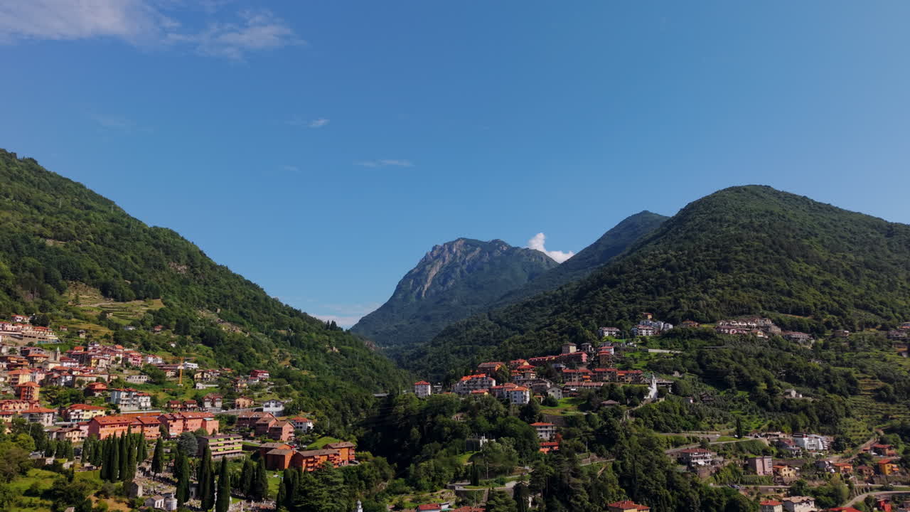 Top-down drone shot tilting up from red rooftops to a football field, the town and the mountains by Lake Como in Italy