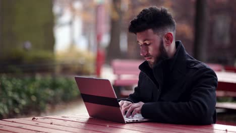 Ein-Junger-Mann-In-Schwarzer-Jacke,-Der-Auf-Dem-Laptop-Im-Tisch-Tippt---Nahaufnahme