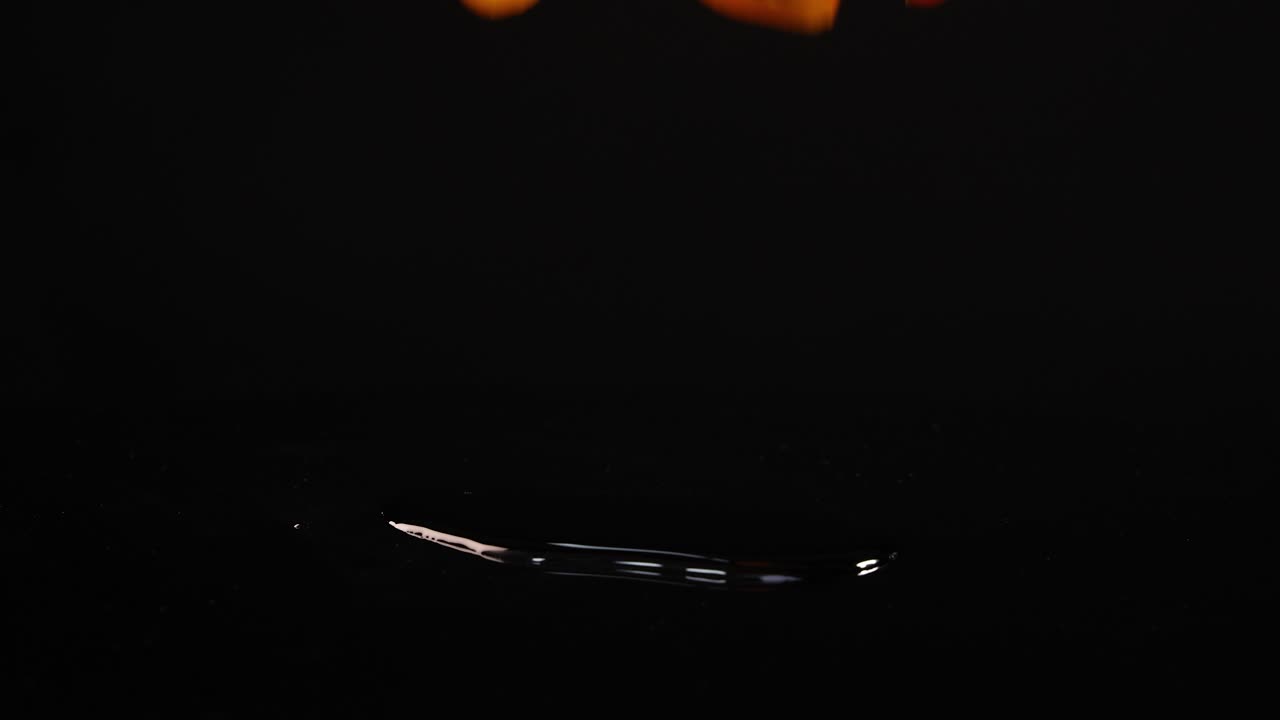 Cherry tomatoes drop and bounce on a reflective black surface, captured in slow motion with dramatic lighting