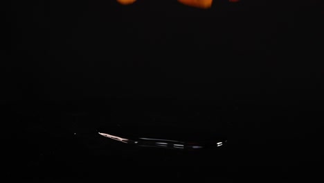 Cherry tomatoes drop and bounce on a reflective black surface, captured in slow motion with dramatic lighting