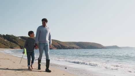 Vater-Und-Sohn-Gehen-Am-Strand-Entlang,-Indem-Sie-Mit-Einem-Fischernetz-Wellen-Am-Strand-Brechen