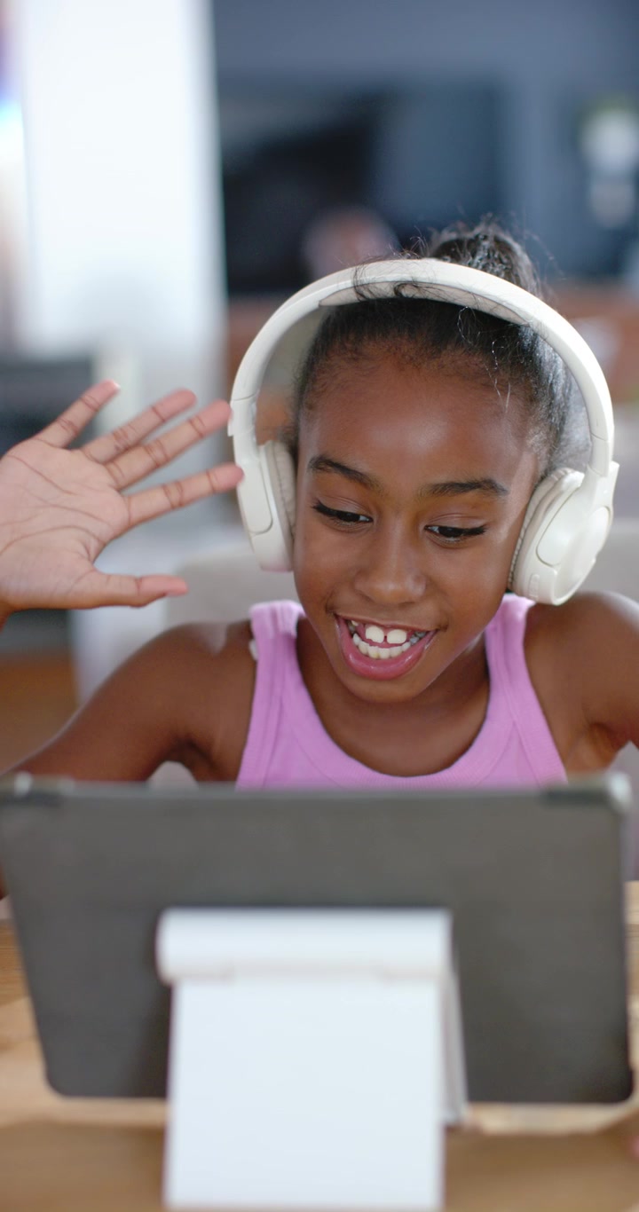 Vertical video: African American child waving as tablet showing call, tapping at table for class