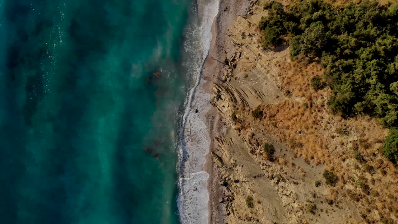 Unspoiled beach on bottom of rocky hills washed by turquoise sea water in Mediterranean, bird's eye view
