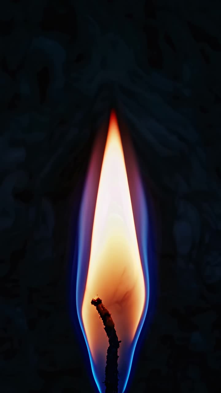 Close-up of a candle flame against a dark background, captured from a side angle