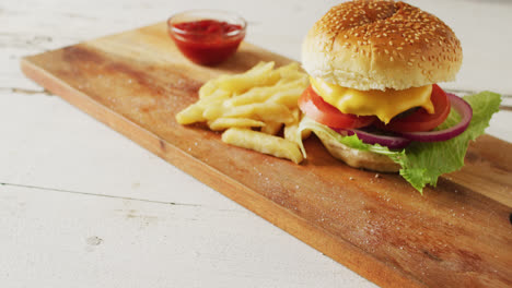video de una hamburguesa con queso, papas fritas y un cuenco de ketchup en una tabla de madera