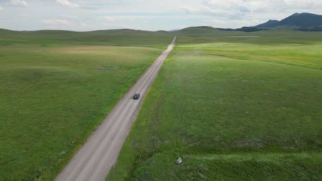 cars pass each other on dirt road surrounded by green grass field on both sides of the road